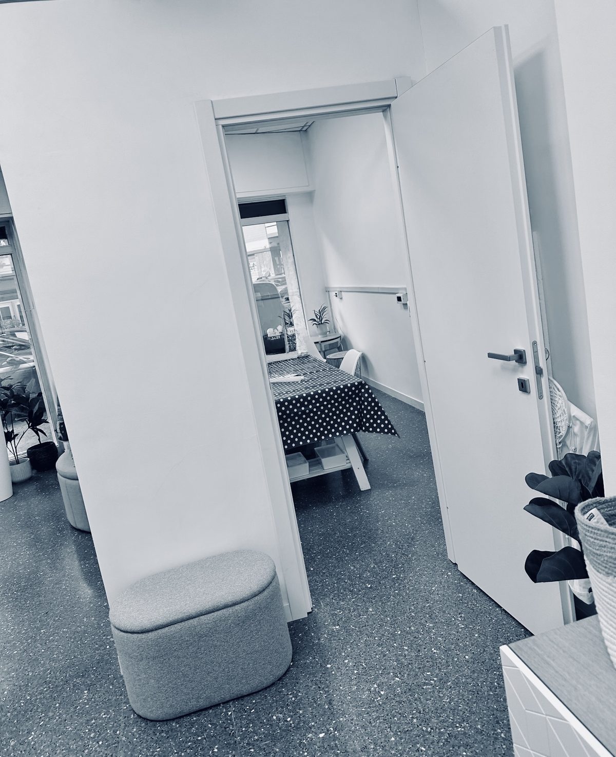 L'interno dell'atelier: pareti bianche, pavimento in graniglia, una porta aperta su una stanza con un tavolo da lavoro e una vetrina sulla strada.